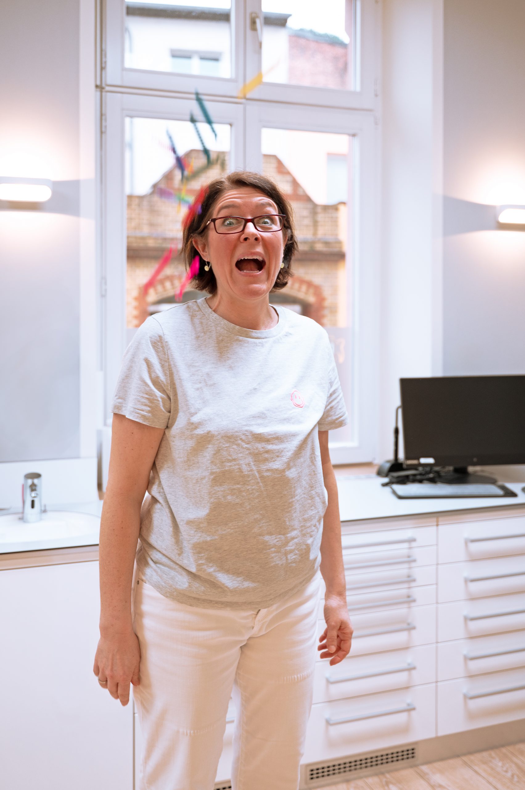 Mitarbeiterin von KFO Dr. Susanne Güntzer steht in einem Praxisszimmer und schaut überrascht in die Kamera.