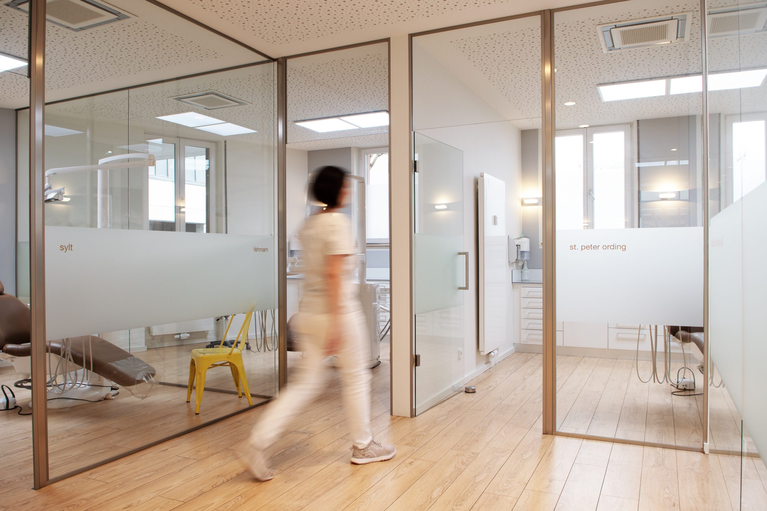 Eine Mitarbeiterin in weißer Arbeitskleidung bewegt sich in ein Praxiszimmer.