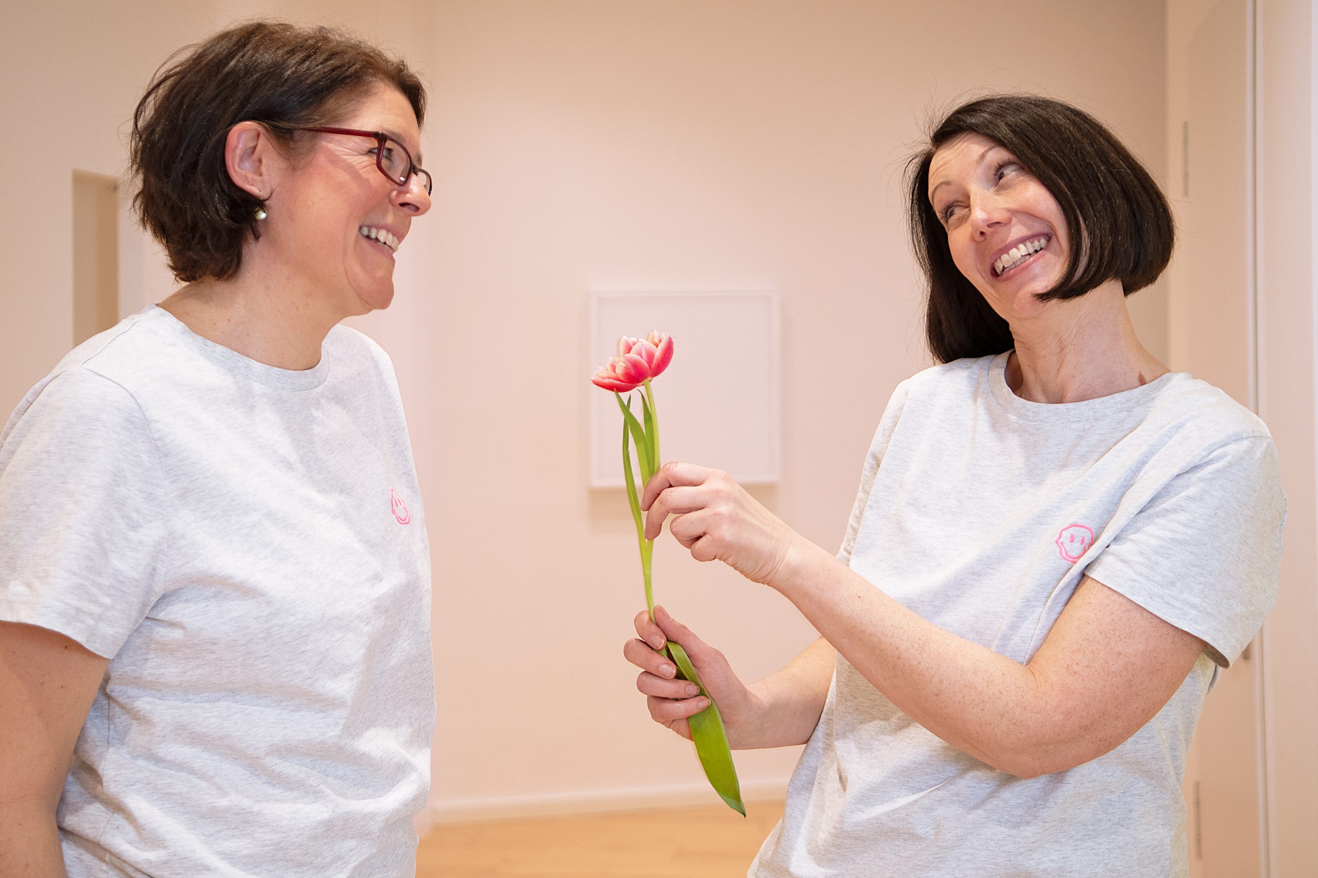 Mitarbeiterin der Praxis für Kieferorthopädie hält eine schöne Blume in der Hand und zeigt diese einer Kollegin